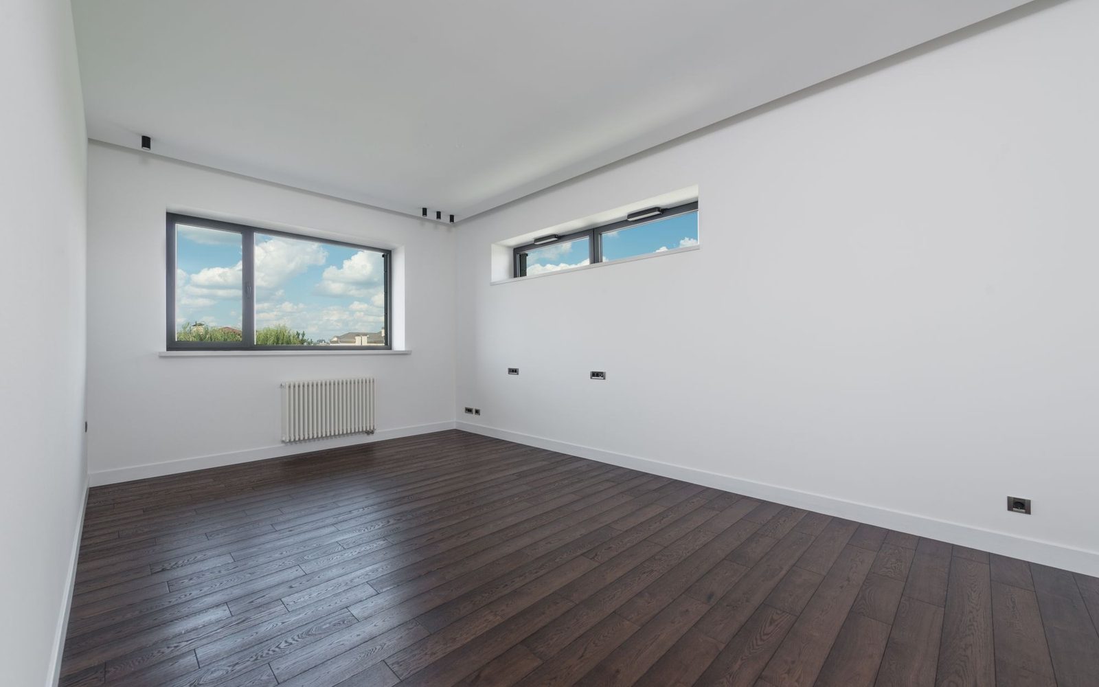 Empty room with dark oak plank flooring and a radiator
